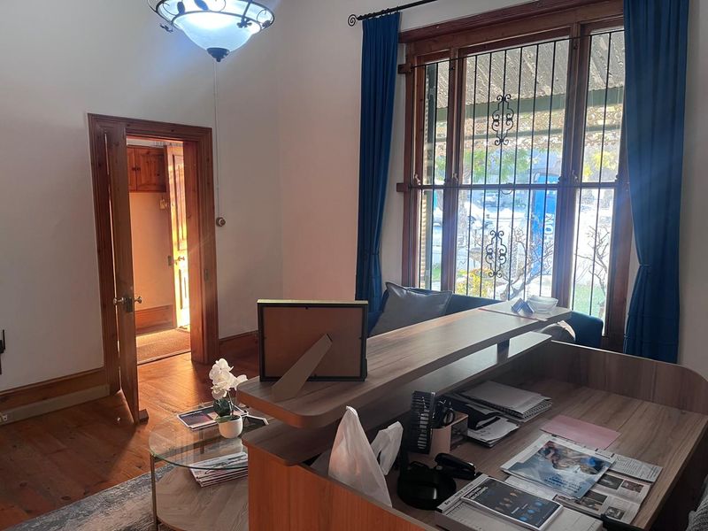 Office space featuring timber flooring, classic timber window frames with security bars, and a doorway leading to an adjacent room.