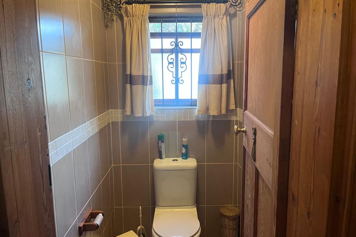 A compact guest bathroom featuring floor-to-ceiling ceramic tiling, a standard toilet, and a window with decorative security bars.