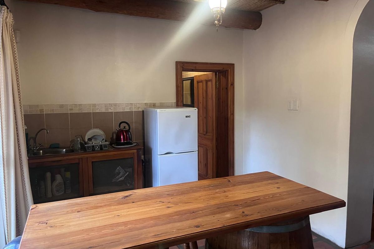 A rustic kitchen area featuring wooden cabinetry, a tiled backsplash, exposed ceiling beams, and terracotta flooring, providing a warm and traditional aesthetic.