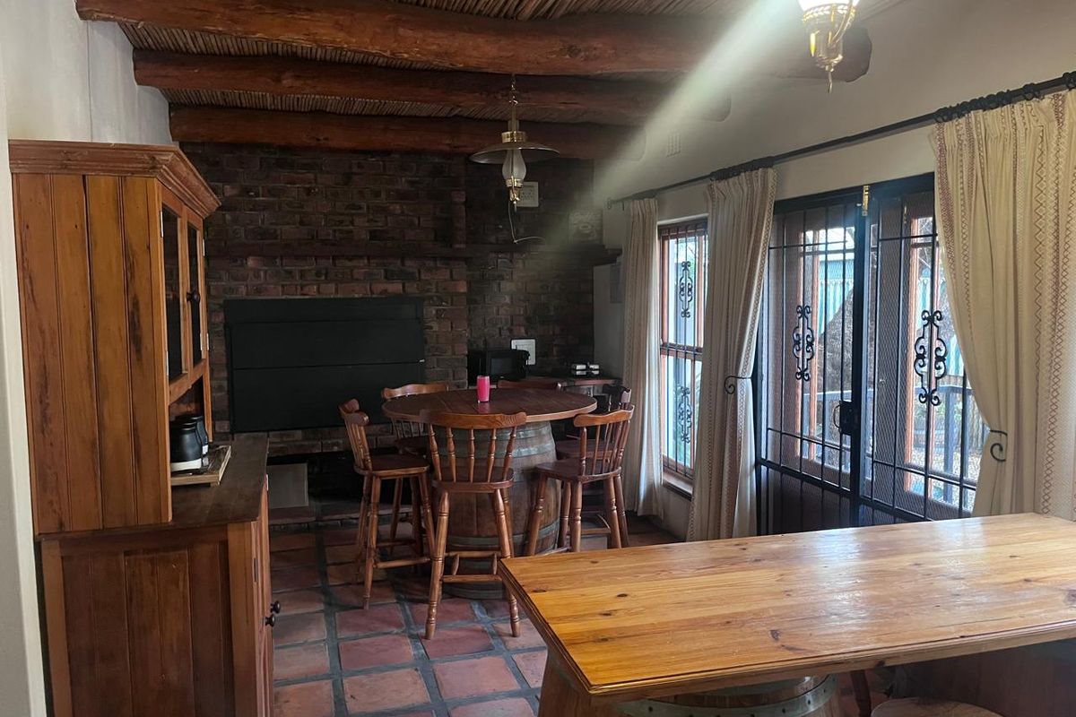 Rustic living area featuring a brick fireplace, exposed timber beam ceiling, and terracotta floor tiles with access to an outdoor area.