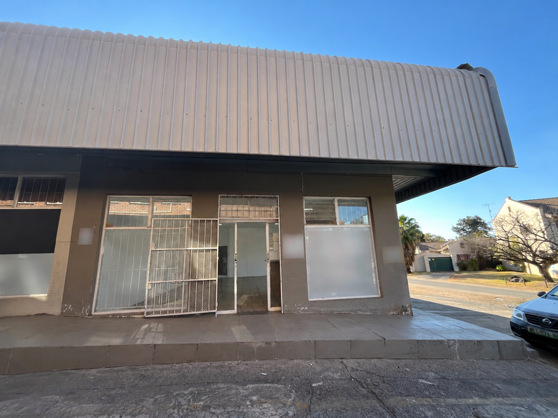 Front facade of a retail property featuring a large metal awning, tiled entrance porch, and glass storefront windows with security gate.