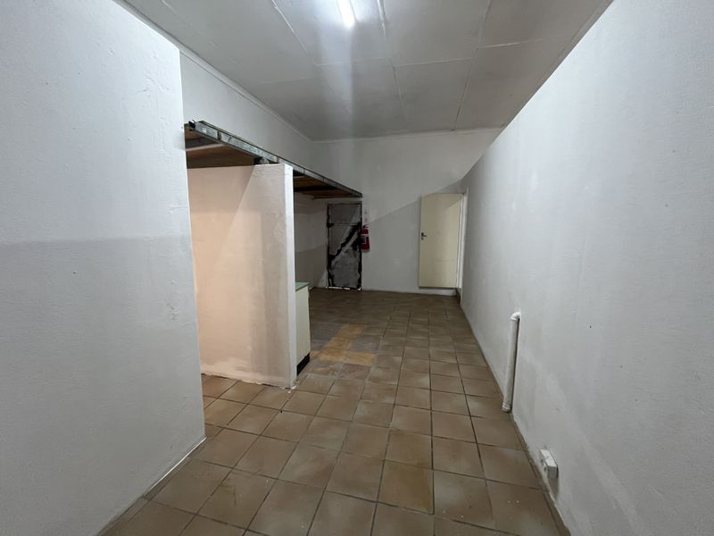 An empty utility or storage space featuring tiled flooring, a partition wall, and basic infrastructure, suitable for various commercial storage or service applications.