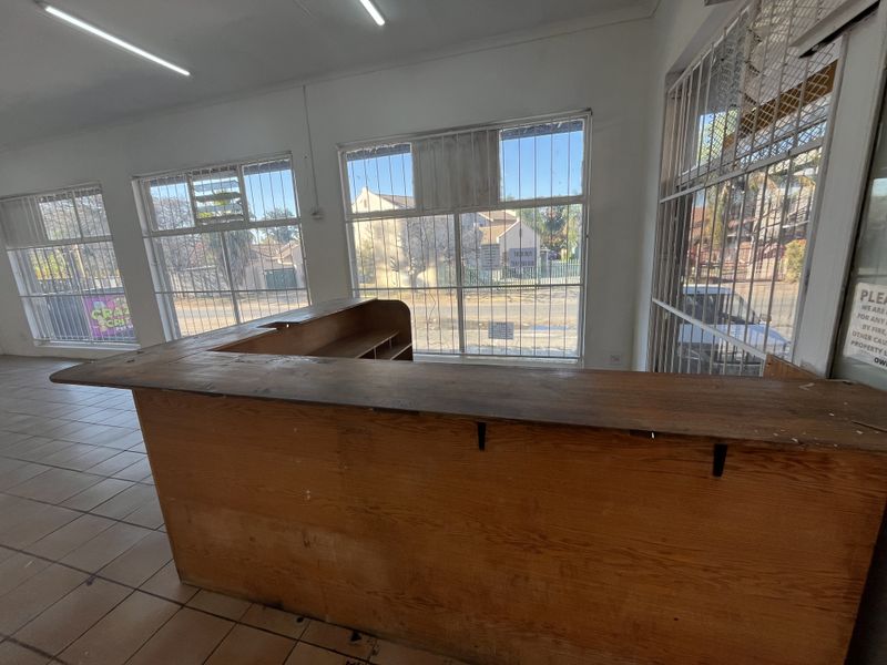 Open plan retail space featuring a built-in wooden service counter, tiled flooring, and large windows with security bars.