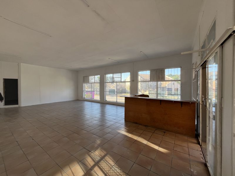 Spacious open-plan retail area featuring tiled flooring, a built-in service counter, and large windows with security bars, offering a versatile commercial layout.