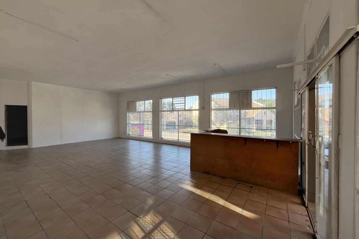 Spacious open-plan retail area featuring tiled flooring, a built-in service counter, and large windows with security bars, offering a versatile commercial layout.