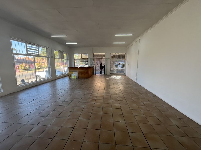 Spacious open-plan retail area featuring large windows with security bars, tiled flooring, and a built-in reception counter, suitable for various commercial business applications.