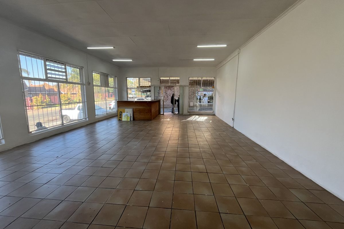 Spacious open-plan retail area featuring large windows with security bars, tiled flooring, and a built-in reception counter, suitable for various commercial business applications.