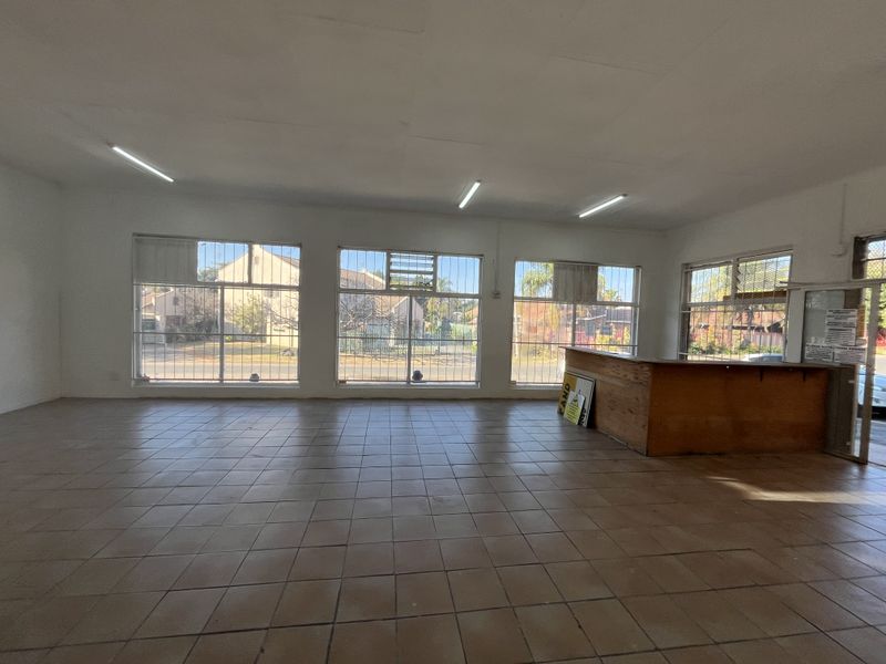 Spacious open-plan retail area featuring large display windows with security bars, tiled flooring, and a built-in service counter, suitable for various commercial uses.