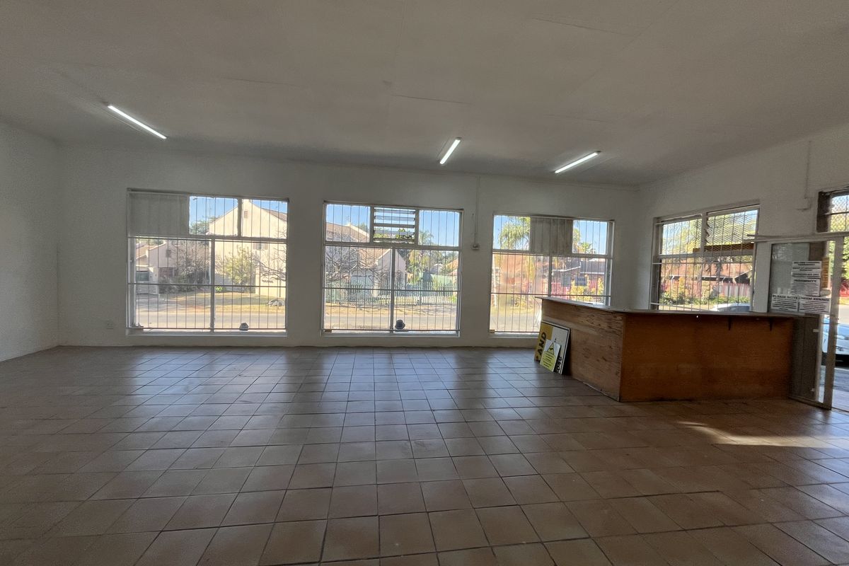 Spacious open-plan retail area featuring large display windows with security bars, tiled flooring, and a built-in service counter, suitable for various commercial uses.