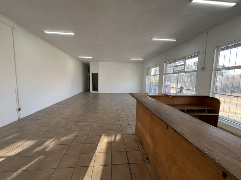 Spacious open-plan retail area featuring tiled flooring, built-in service counter, and large windows with security bars, offering a versatile commercial layout.