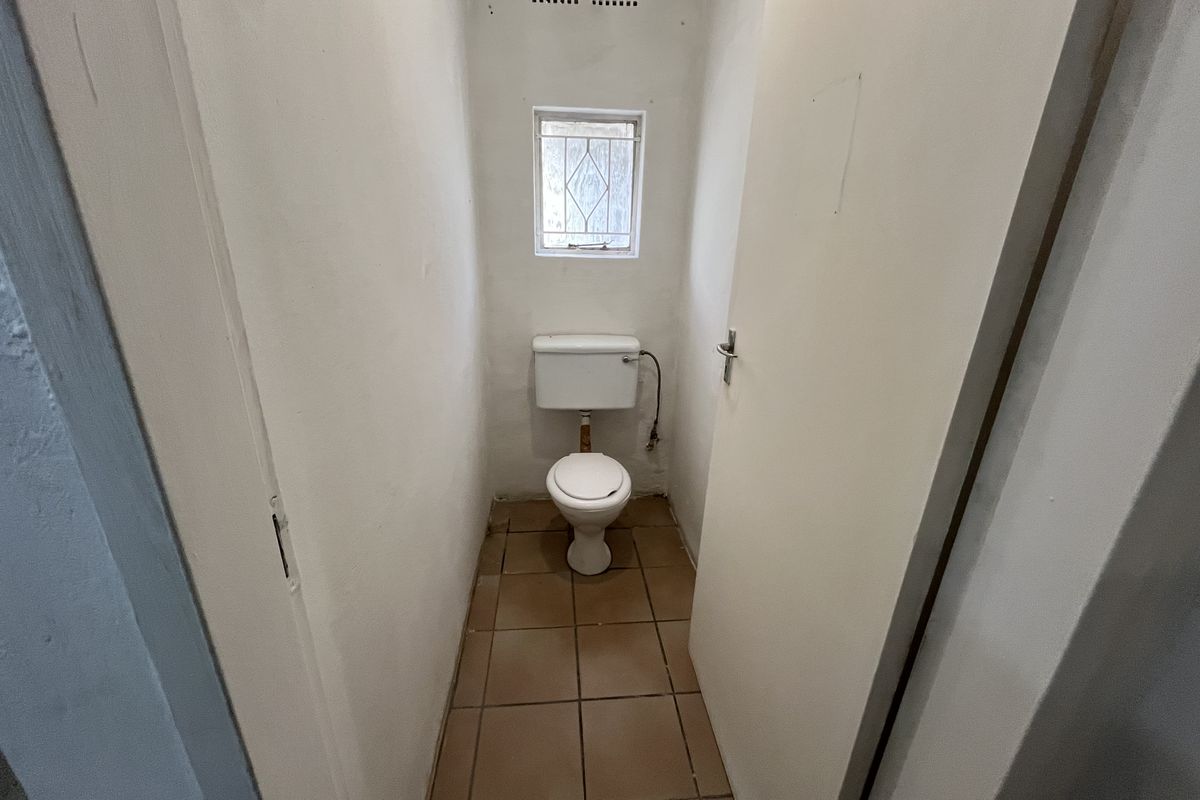 A compact, functional restroom featuring a standard toilet, tiled flooring, and a small window with security bars.