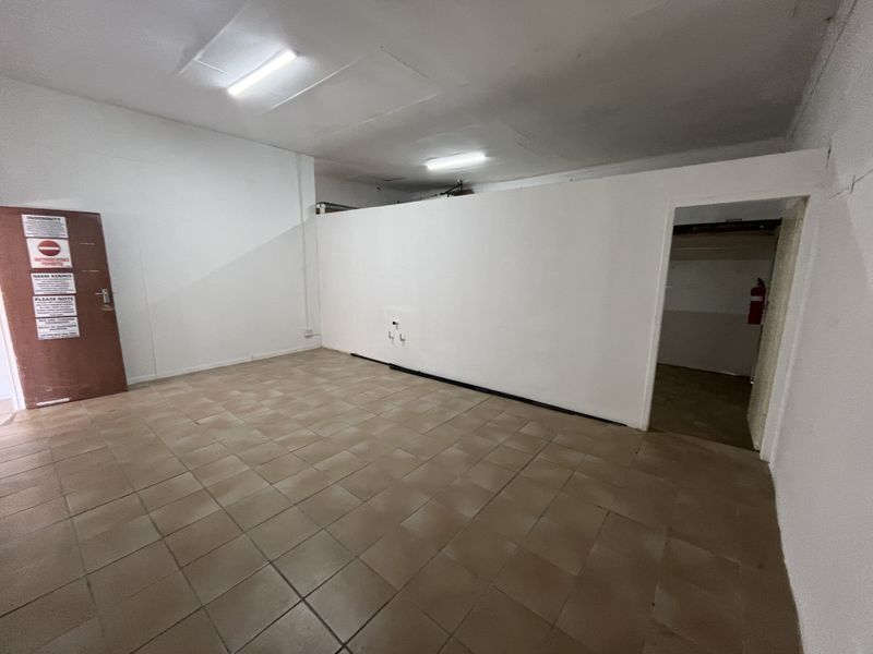 An empty utility or storage space featuring tiled flooring, fluorescent lighting, and a partition wall, suitable for various commercial or storage applications.