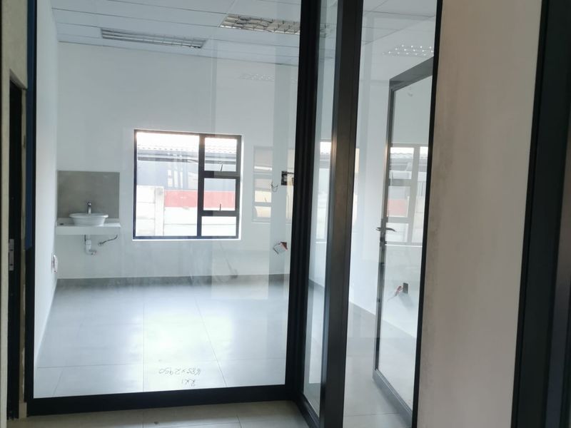 A modern, empty office space featuring glass partitions, tiled flooring, a suspended ceiling, and a private wall-mounted basin.