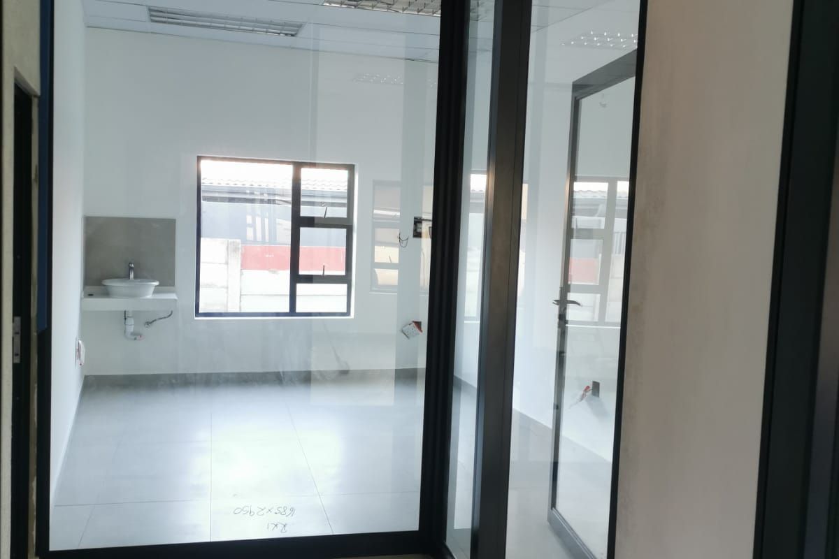 A modern, empty office space featuring glass partitions, tiled flooring, a suspended ceiling, and a private wall-mounted basin.