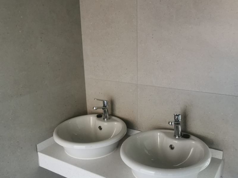 A modern bathroom featuring a double vanity with ceramic basins, chrome faucets, and a stone countertop set against large format neutral wall tiles.