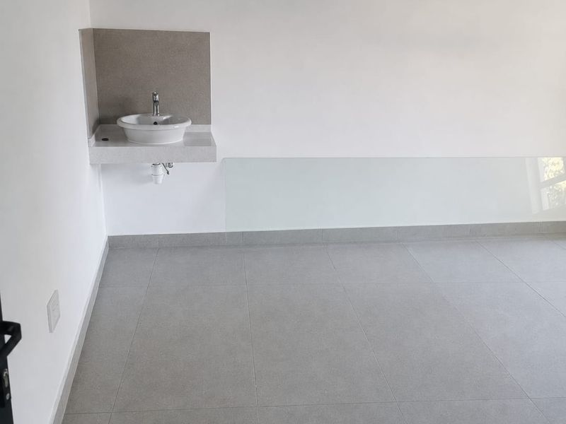 A clean, minimalist utility space featuring large-format grey floor tiles, a wall-mounted basin with a modern faucet, and a sleek glass splashback.