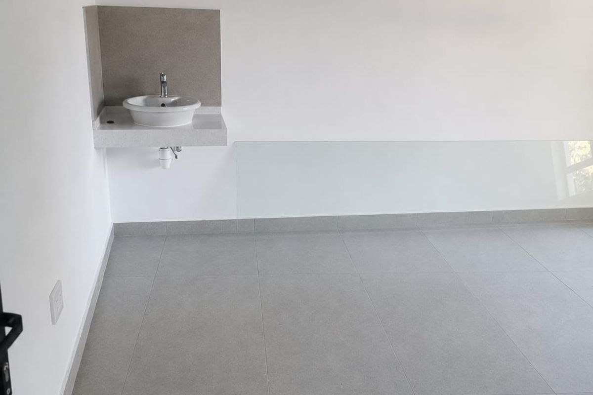A clean, minimalist utility space featuring large-format grey floor tiles, a wall-mounted basin with a modern faucet, and a sleek glass splashback.