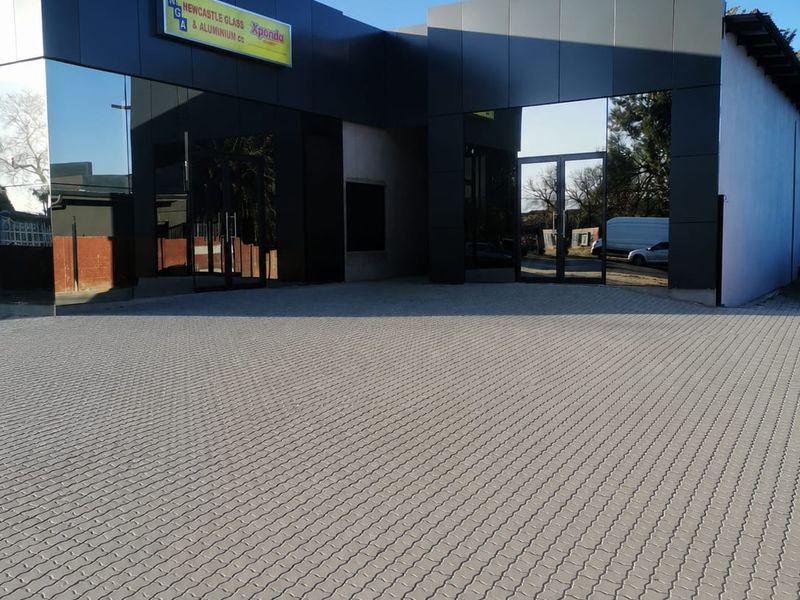 Modern commercial building exterior featuring a paved driveway, sleek dark aluminium cladding, and large glass facade panels with prominent signage.