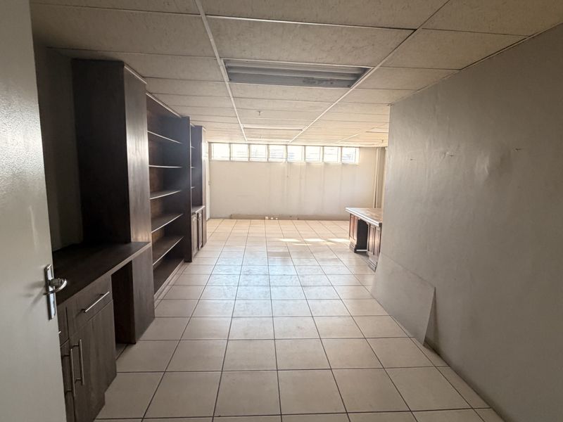 A functional office space featuring tiled flooring, built-in cabinetry, and natural light from high-level windows, suitable for a professional work environment.