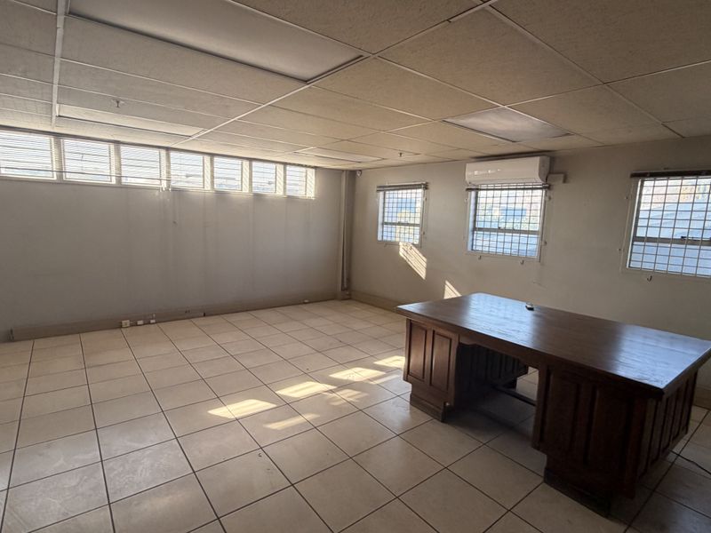 Spacious commercial office area featuring tiled flooring, suspended ceiling, security bars on windows, and a wall-mounted air conditioning unit.