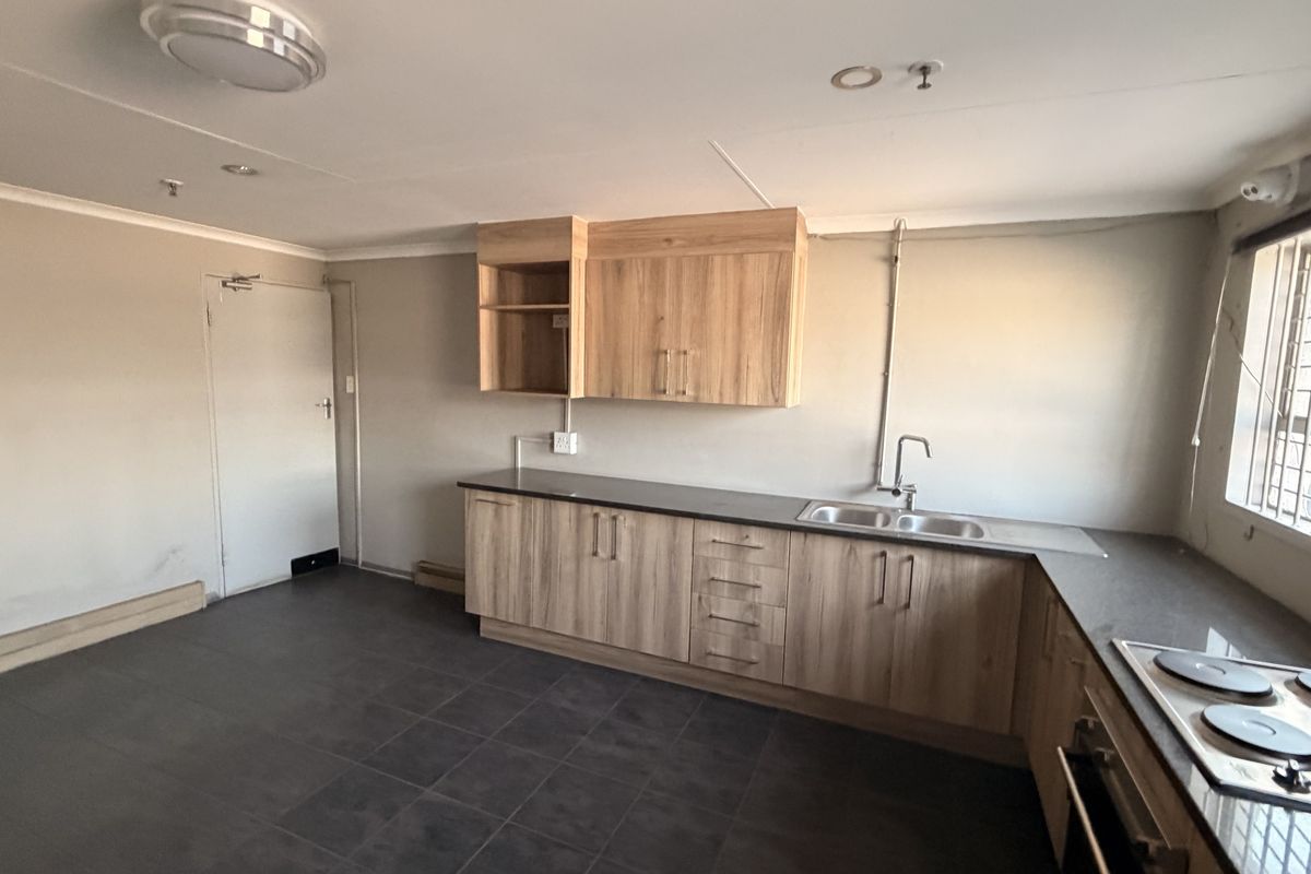 A functional kitchen featuring wood-look cabinetry, dark countertops, a built-in hob and oven, and a double sink with security bars on the window.