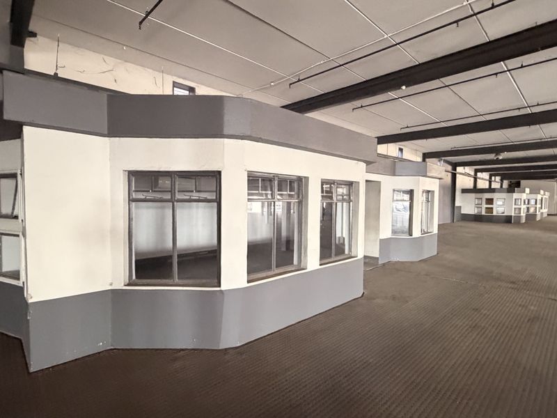 Expansive open-plan commercial space featuring built-in partitioned office structures, exposed steel beams, and a suspended ceiling, suitable for versatile business use.