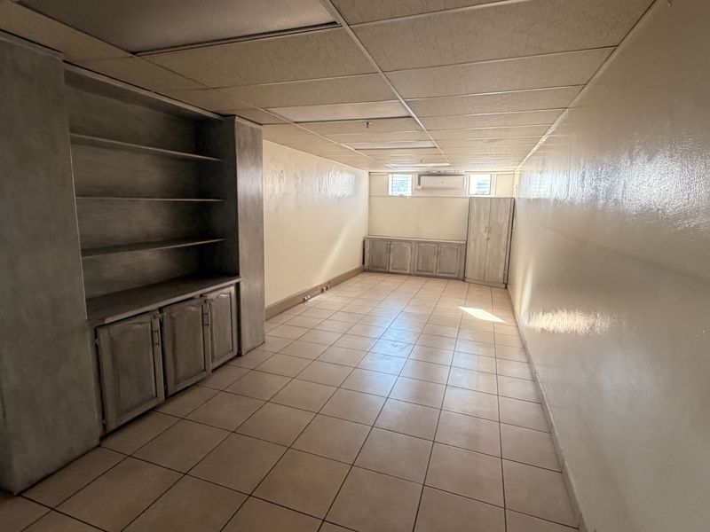 An empty commercial office space featuring tiled flooring, a drop ceiling, built-in storage cabinetry, and a wall-mounted air conditioning unit.