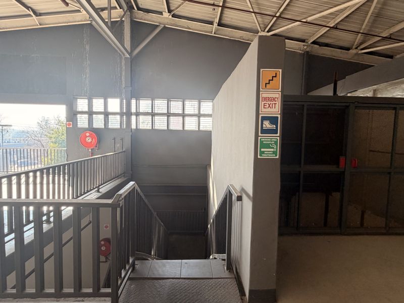 Industrial utility area featuring a metal staircase, freight elevator, and exposed steel roof structure with emergency exit signage.