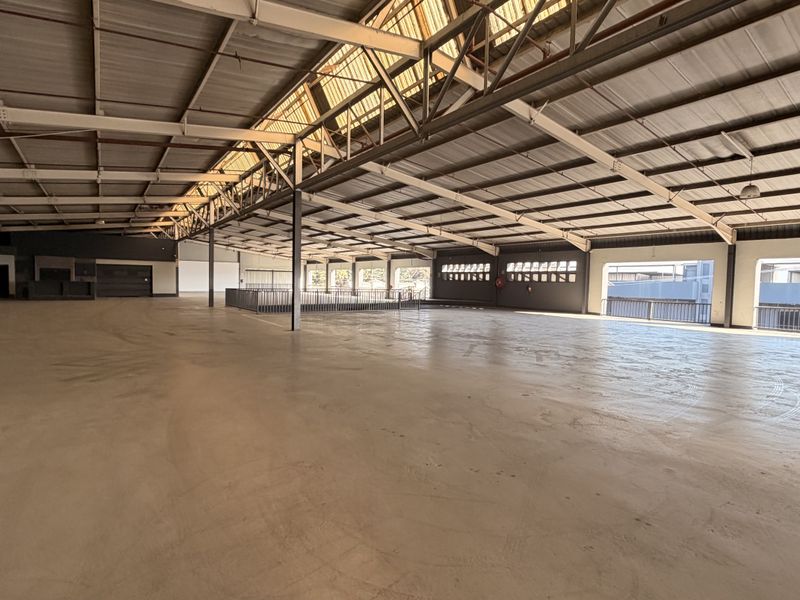 Expansive open-plan commercial warehouse space featuring high ceilings with exposed steel trusses, natural light from skylights, and durable concrete flooring.