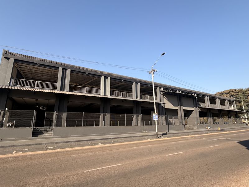 A modern commercial building featuring a dark grey steel structural frame, multi-level balconies, and perimeter security fencing along the street front.