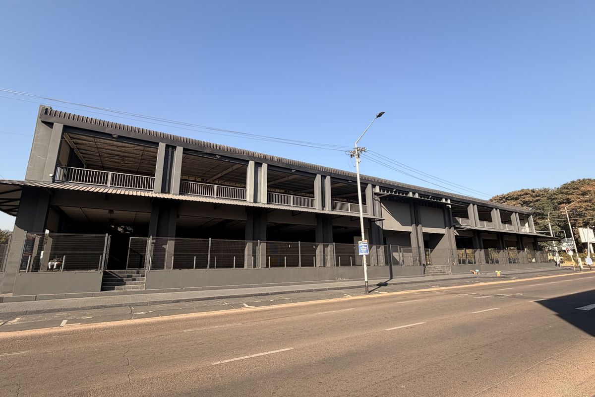 A modern commercial building featuring a dark grey steel structural frame, multi-level balconies, and perimeter security fencing along the street front.