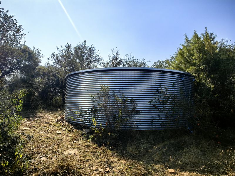 A large corrugated steel water storage tank situated in a rural garden setting, providing essential water infrastructure for the property.