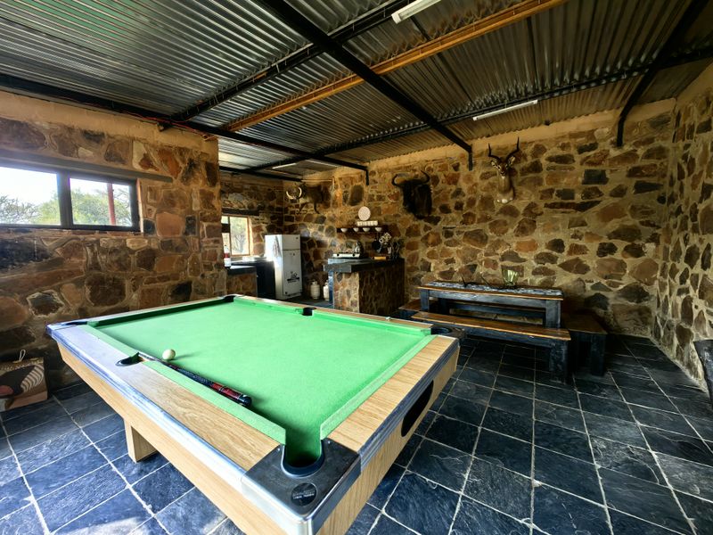 Rustic outdoor entertainment area featuring stone walls, slate flooring, and a corrugated metal roof, currently set up as a recreational space.