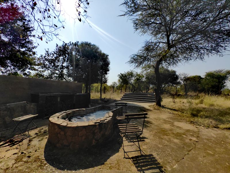 Outdoor entertainment area featuring a stone fire pit, built-in braai, and concrete patio space set within a natural farm landscape.