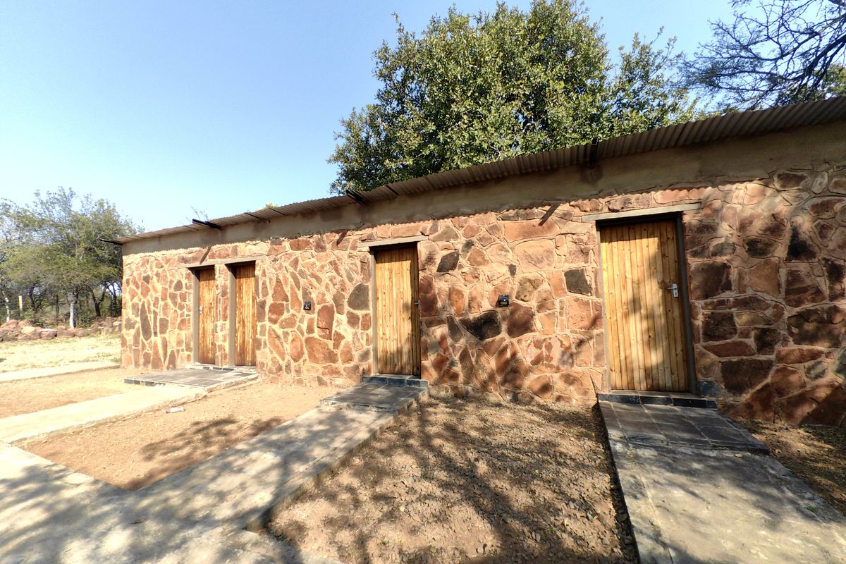 Exterior view of a rustic stone-clad farm building featuring multiple timber entrance doors and concrete pathways under a corrugated metal roof.