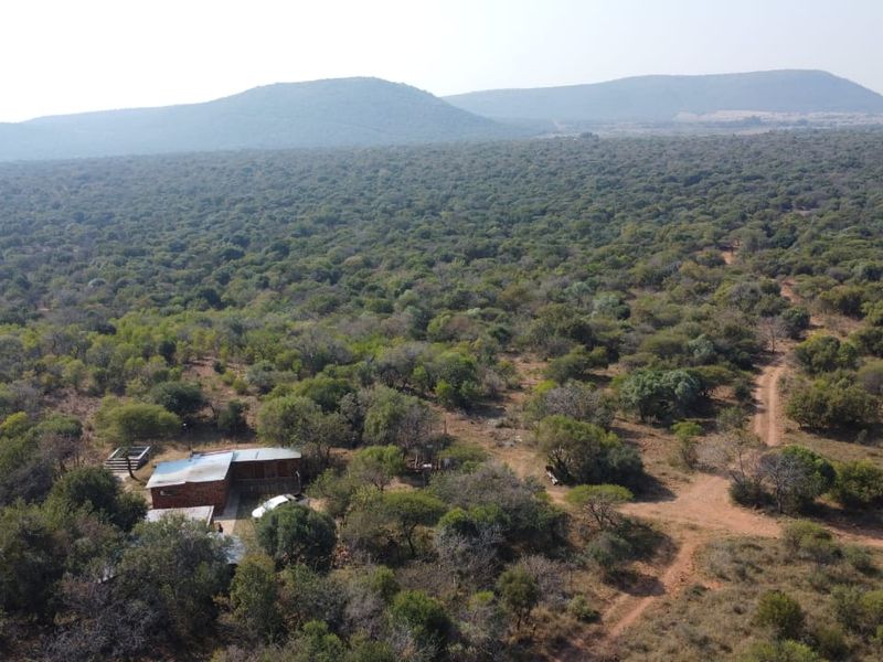 An aerial view of a rural farm property surrounded by extensive natural bushveld and rolling hills.