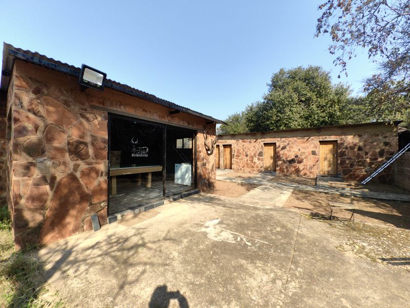 Rear view of a rustic stone-clad farm building featuring a concrete patio, sliding glass doors, and multiple wooden access doors.