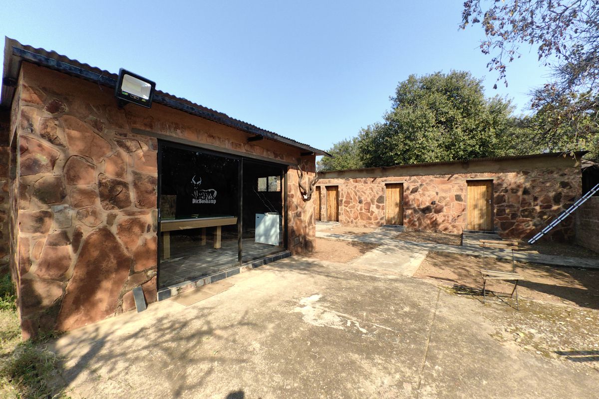 Rear view of a rustic stone-clad farm building featuring a concrete patio, sliding glass doors, and multiple wooden access doors.