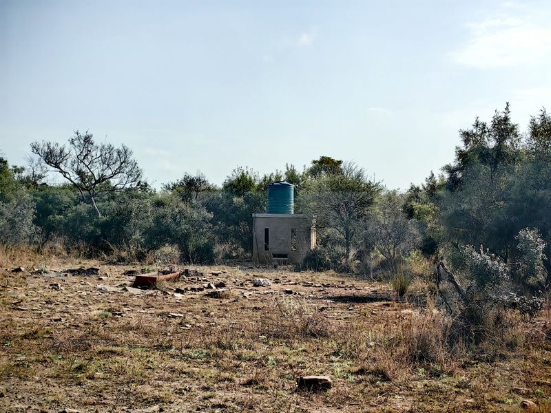 A rural farm landscape featuring a concrete structure topped with a water storage tank, surrounded by natural vegetation and dry terrain.