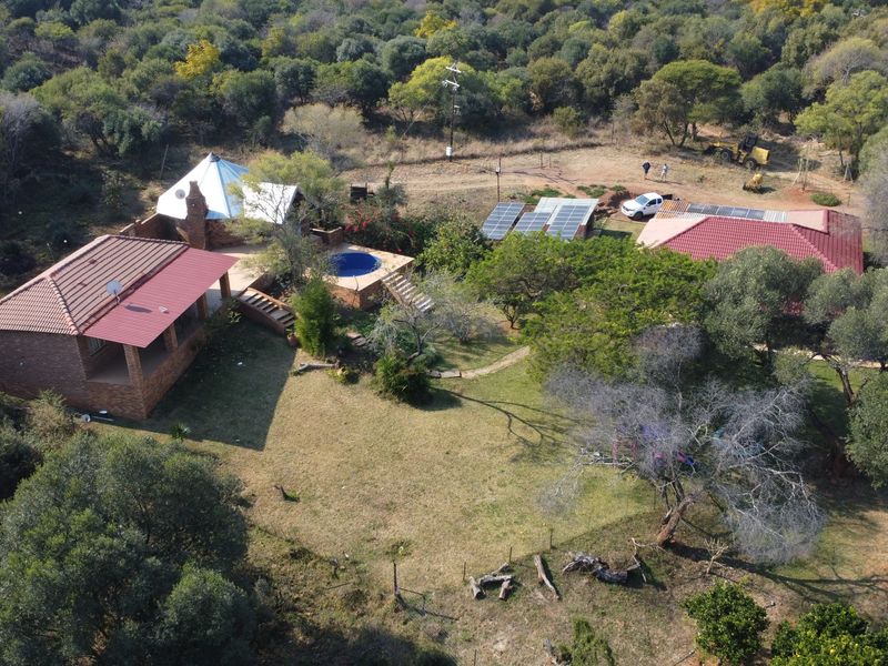 Aerial view of a farm property featuring multiple buildings, a swimming pool, and a solar panel installation set within a natural bushveld landscape.