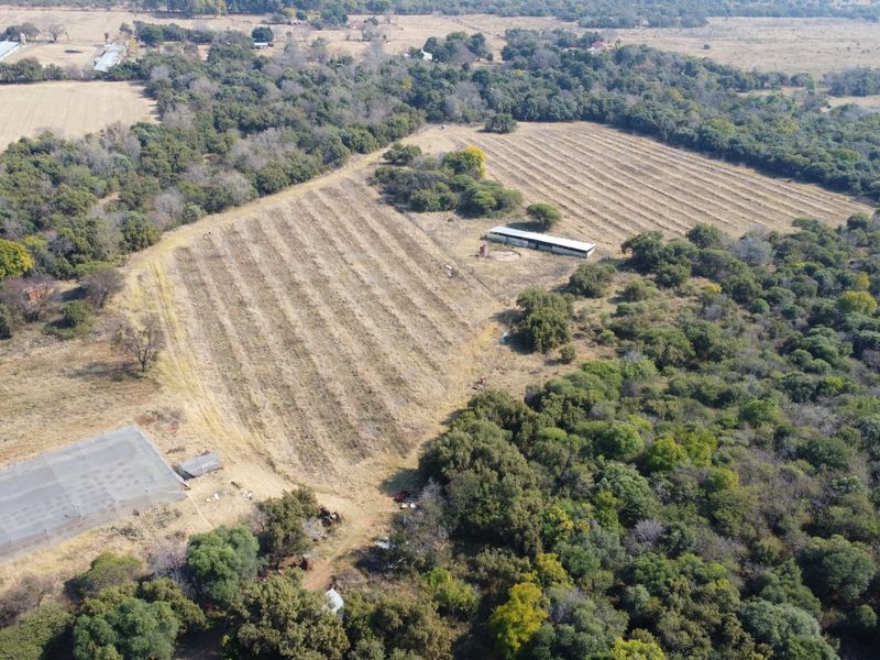 Aerial view of a large farm property featuring extensive agricultural land, natural woodland, and existing outbuildings with shade netting structures.