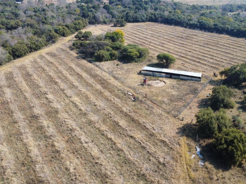 Aerial view of a farm property featuring agricultural land, a fenced enclosure, an outbuilding, and a water tank.