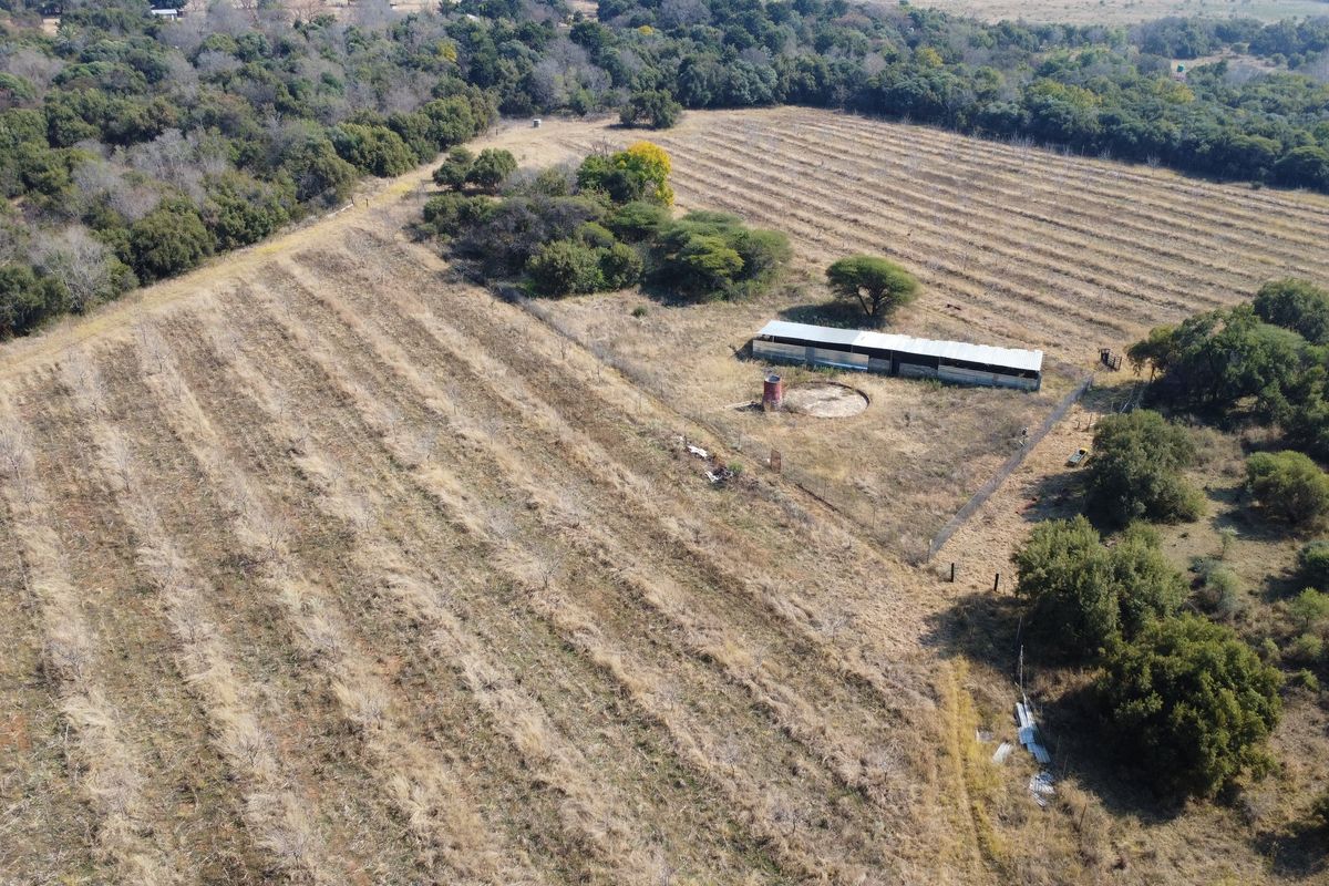 Aerial view of a farm property featuring agricultural land, a fenced enclosure, an outbuilding, and a water tank.