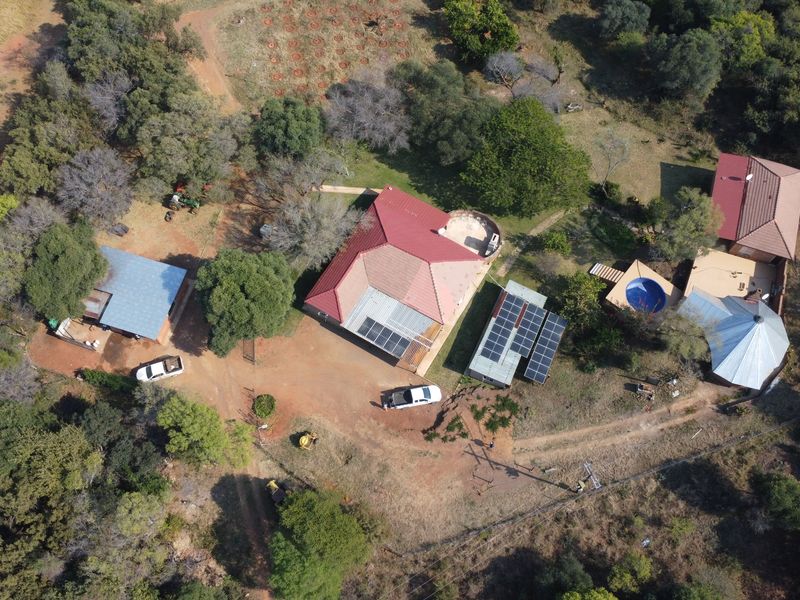Aerial view of a farm property featuring multiple buildings, solar panel installations, a swimming pool, and surrounding natural landscape.