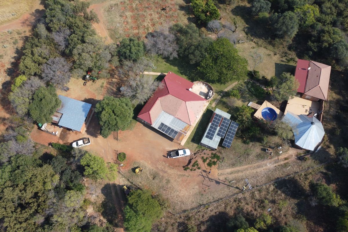 Aerial view of a farm property featuring multiple buildings, solar panel installations, a swimming pool, and surrounding natural landscape.