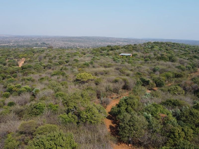 An aerial view of a vast, undeveloped farm landscape featuring natural bushveld vegetation and a dirt access track.