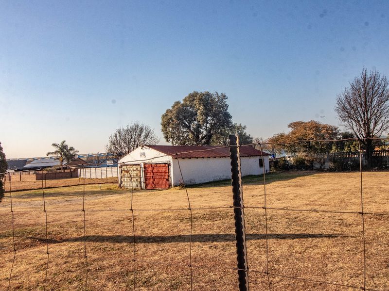 A view of a detached garage structure with metal doors, situated on a large plot of land enclosed by wire fencing.