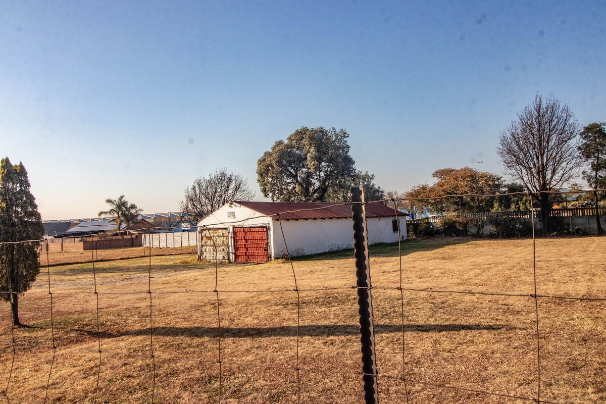 A view of a detached garage structure with metal doors, situated on a large plot of land enclosed by wire fencing.