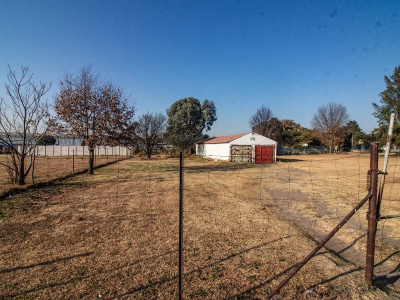 A view of a large commercial plot featuring a detached garage structure with metal doors, enclosed by wire mesh fencing.