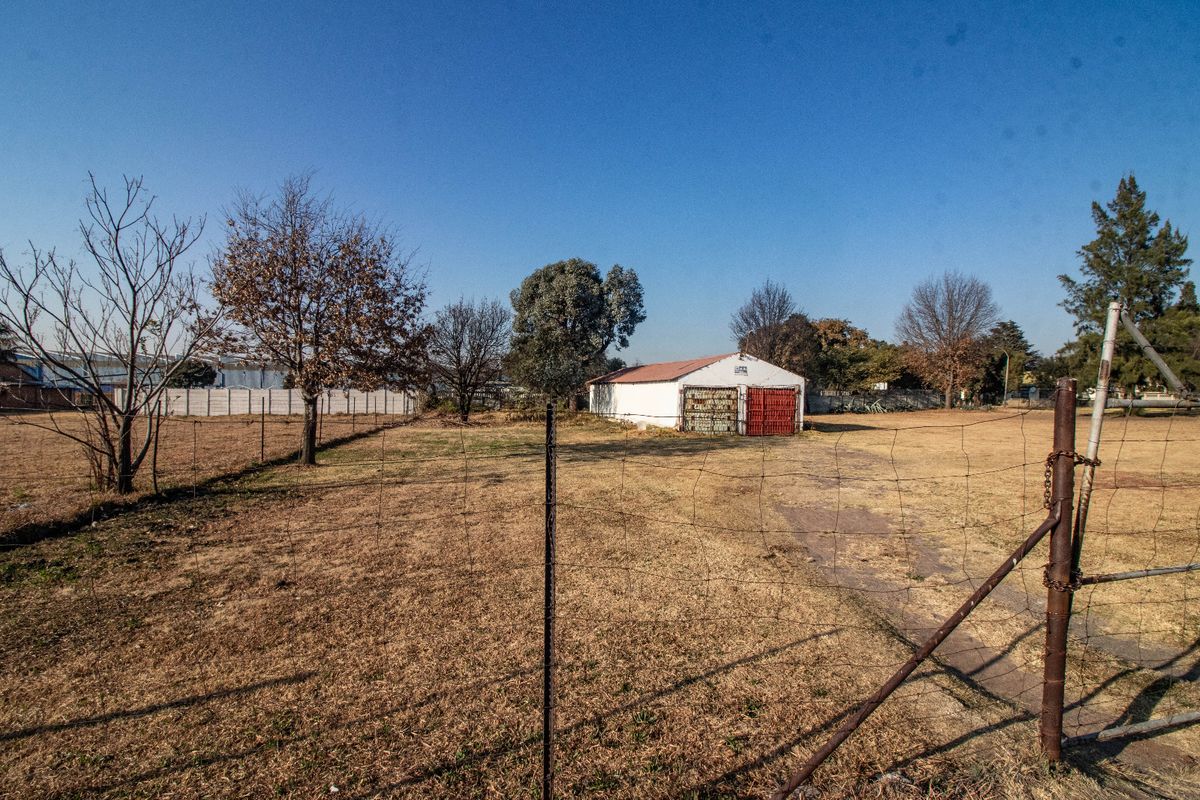 A view of a large commercial plot featuring a detached garage structure with metal doors, enclosed by wire mesh fencing.